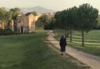 Photo of an older woman walking along a path to a village of stone buildings