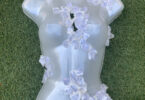 An opaque plastic female body form with large crystal-like shapes lies on grass.