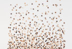 Dots in variations of cream to brown on a plain background and are denser to the bottom as they disperse upwards.