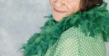 A woman smiles over her shoulder at the viewer while wearing a green boa and green blouse.