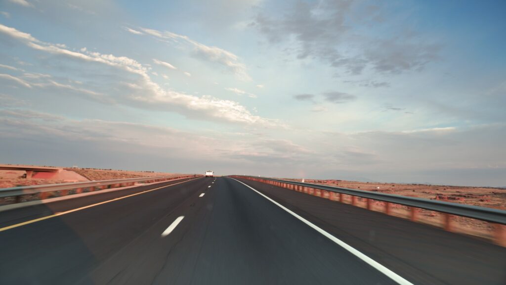 Photograph of a long straight road to the horizon with a pale blue sky with clouds.  