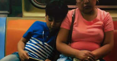 A young boy leans on a woman's shoulder while sitting on the train.