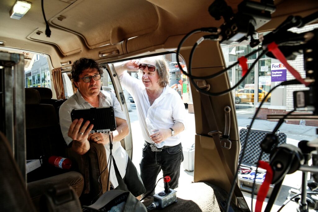 Photo of the two men by their van, showing some of the technical seup inside the van.  