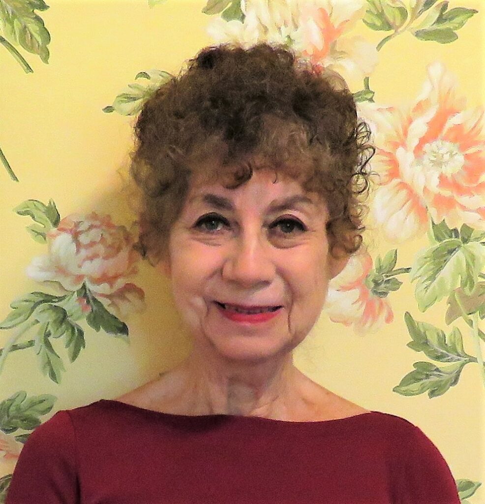 A woman smiles at the viewer against a floral background.