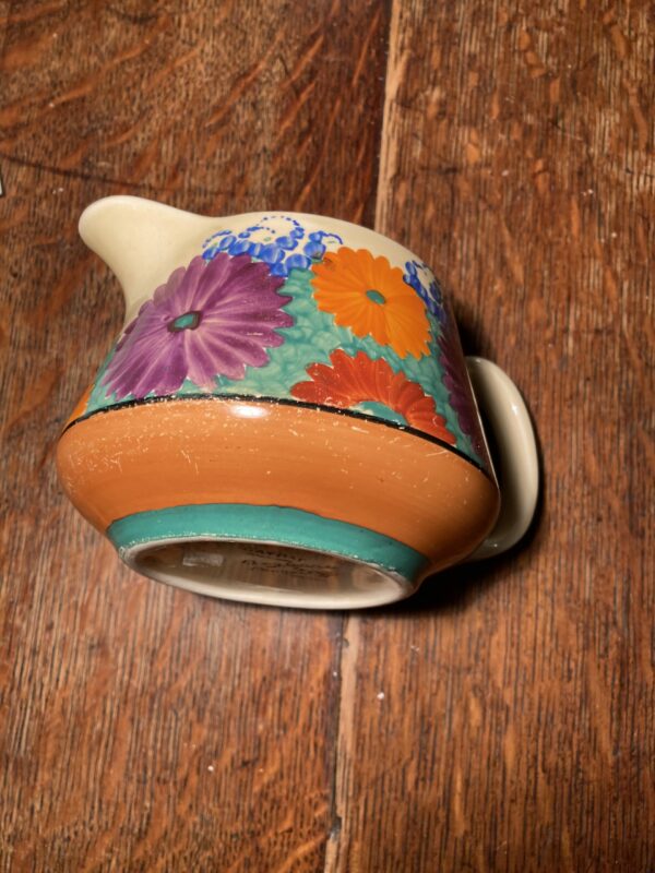 round squat jug on its side with bright daisy like flowers on a green grass packground - jug is on a wooden floor.